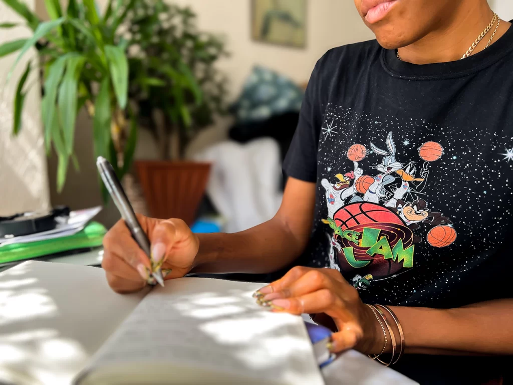 Black woman journaling by a window with soft light — calming and reflective energy
