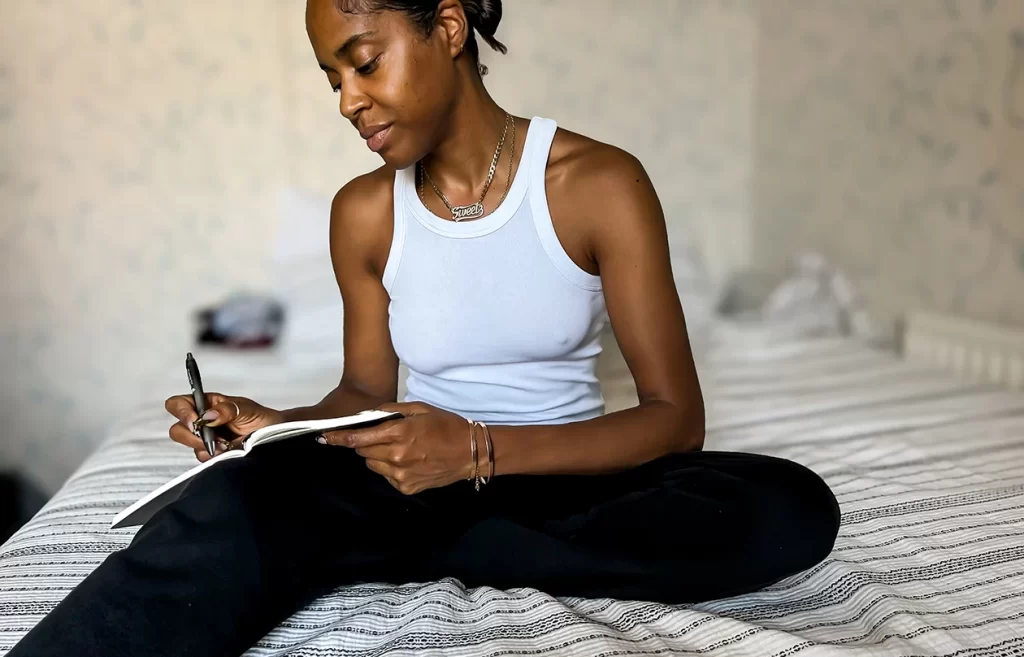 Black woman sitting peacefully by a window with journal in lap and tea in hand